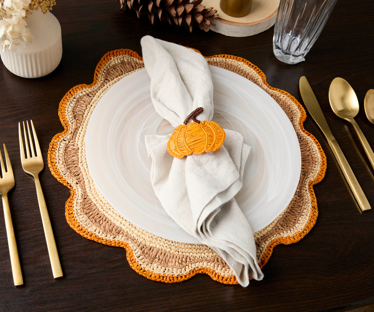 Round raffia woven placemat in crochet style with orange and natural tones, set on a dark wooden table with gold utensils.