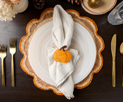 Round raffia woven placemat with a scalloped edge, featuring natural fibers and an orange accent, set on a dining table.