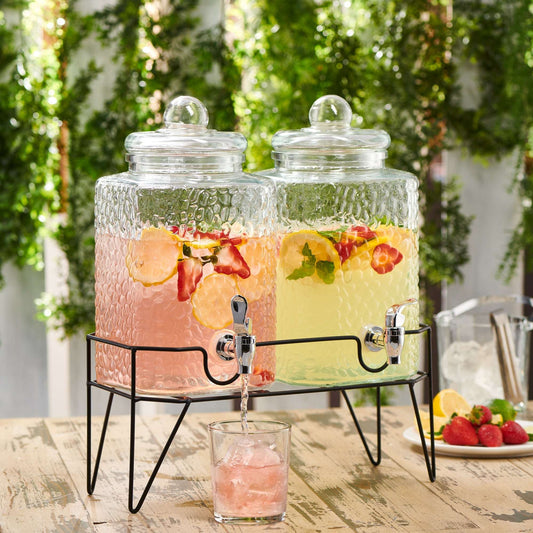 Two textured glass beverage dispensers with metal spigots on a black metal stand, filled with fruit-infused drinks.
