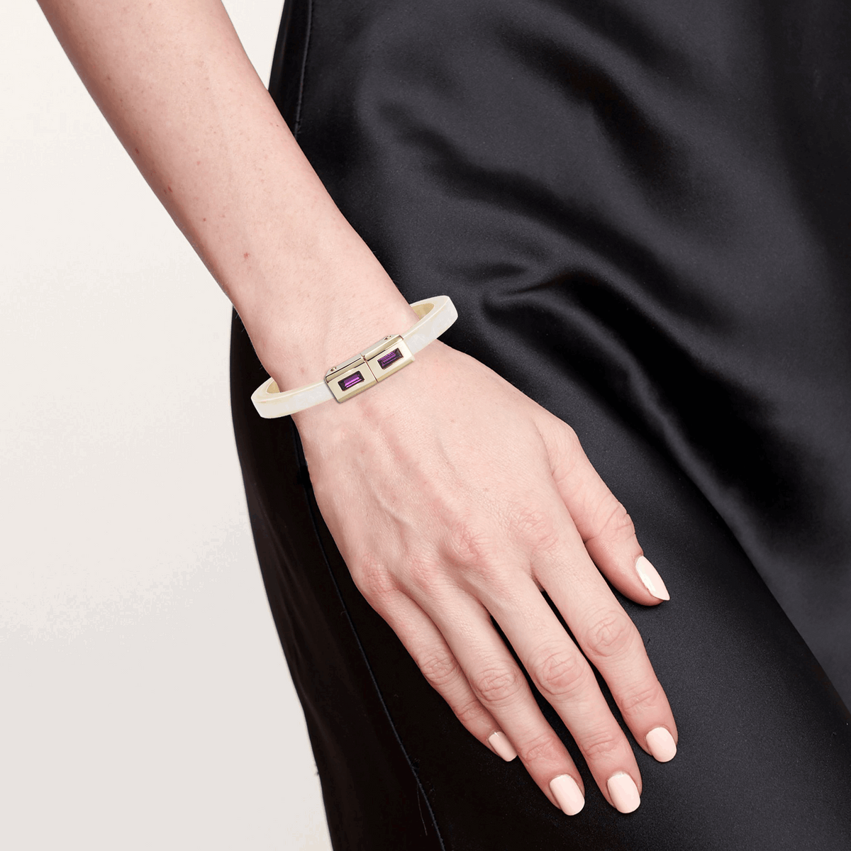 Hand wearing a white bracelet with a gold tag against a black background