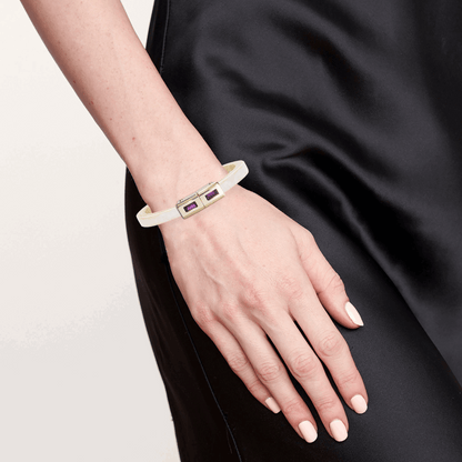 Hand wearing a white bracelet with a gold tag against a black background