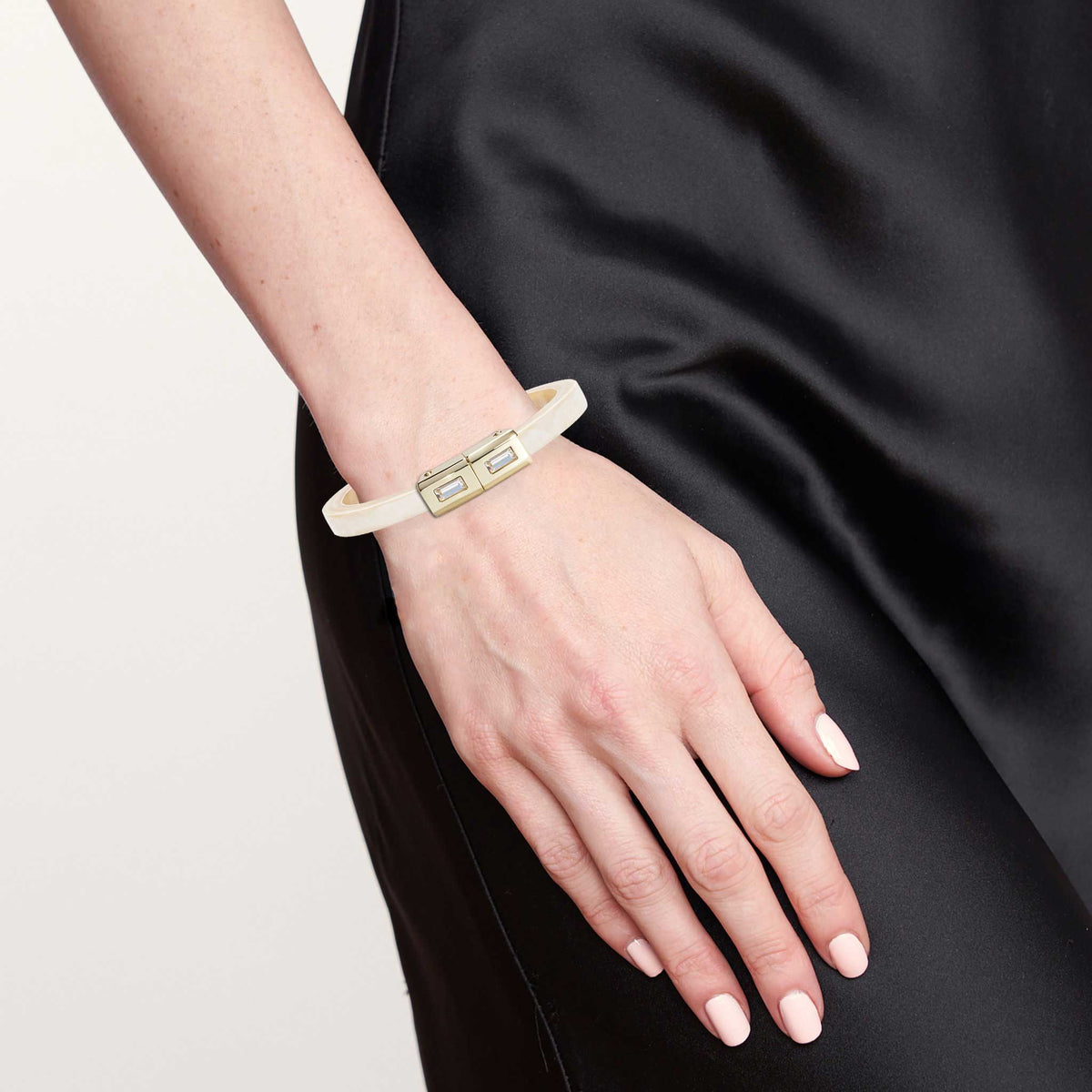 Hand wearing a white bracelet with a gold tag against a black background