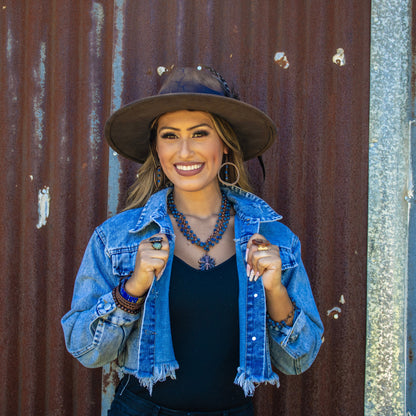 Woman wearing a denim jacket and hat against a rusty metal wall