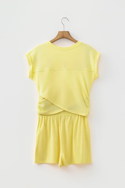 A two-piece matching lounge set in pale yellow, featuring a short-sleeve top with a wrap-style front and matching shorts, hanging on a wooden hanger against a plain white wall.