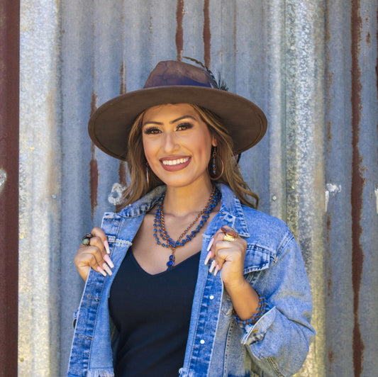 Woman wearing a denim jacket and brown hat against a corrugated metal background