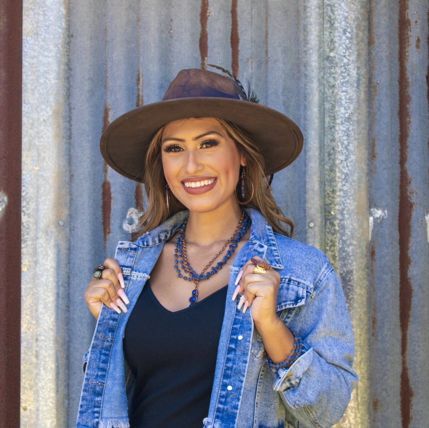 Woman wearing a denim jacket and brown hat against a corrugated metal background