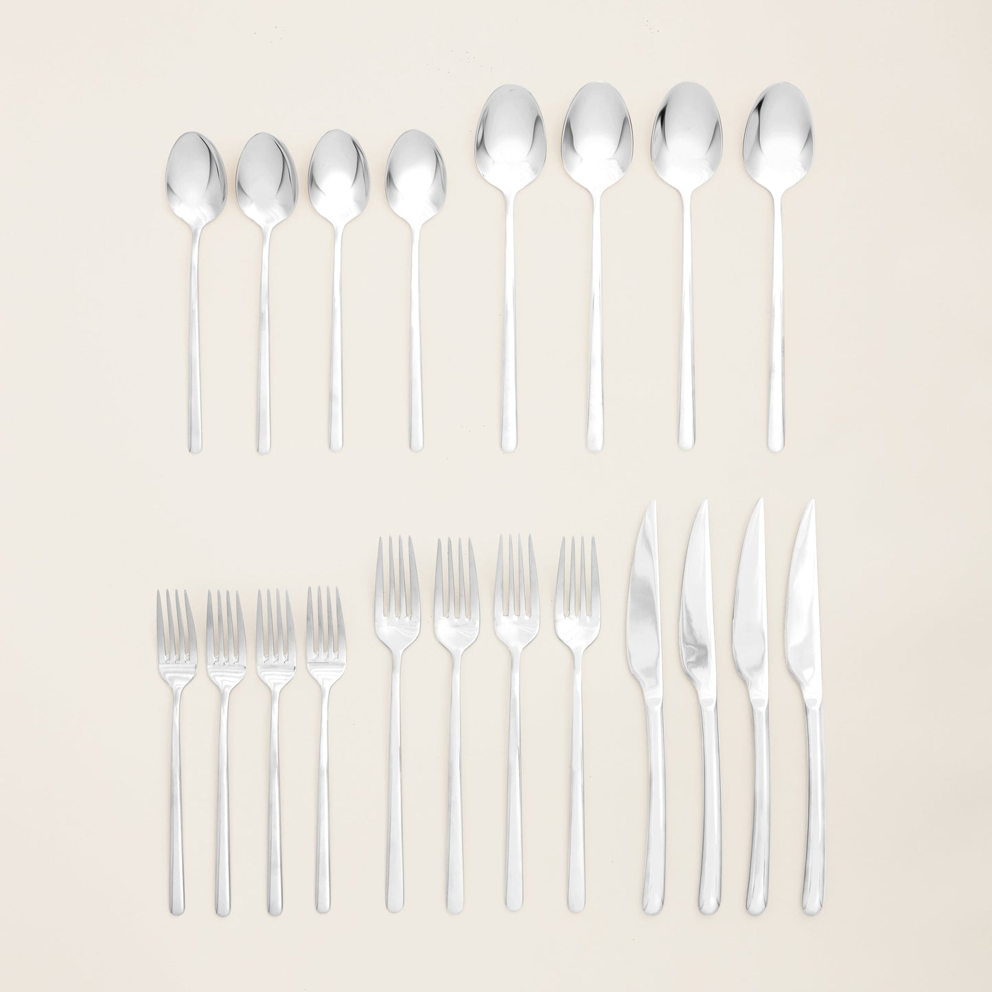 Set of silver cutlery including spoons, forks, and knives on a beige background