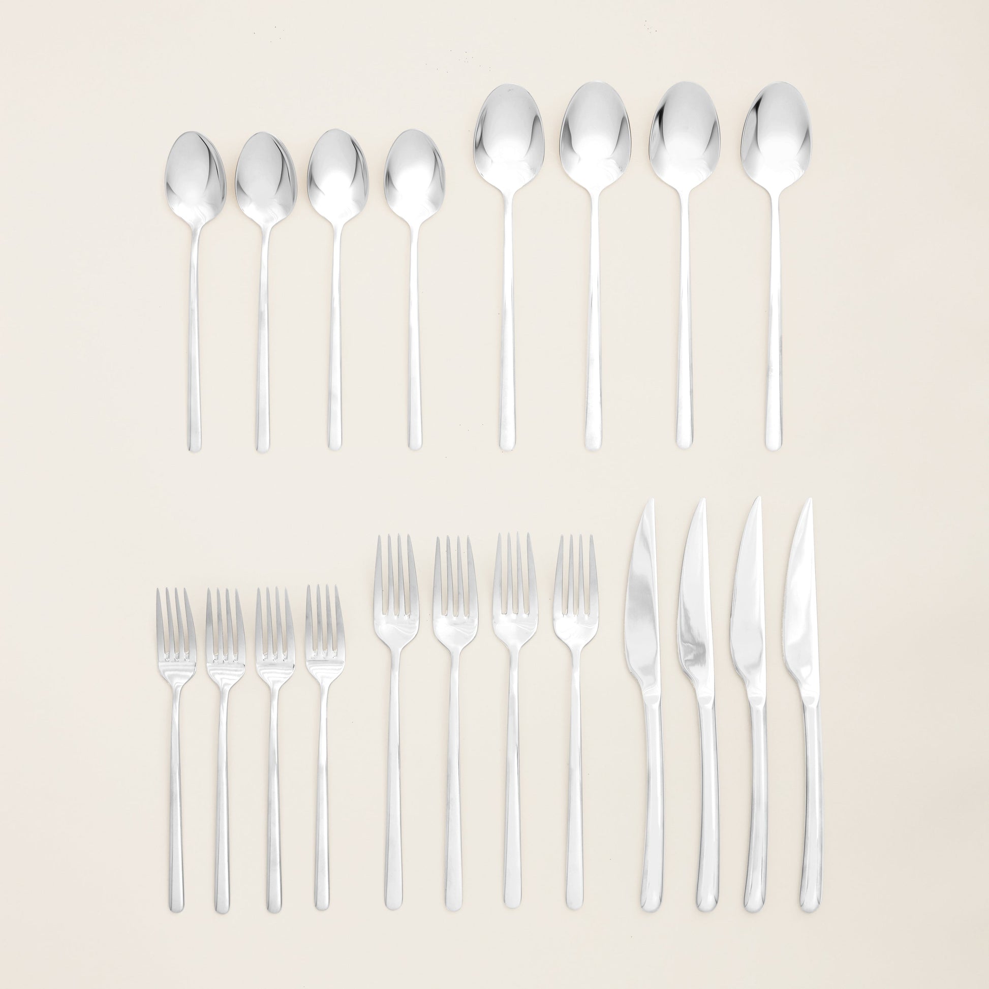 Set of silver cutlery including spoons, forks, and knives on a beige background