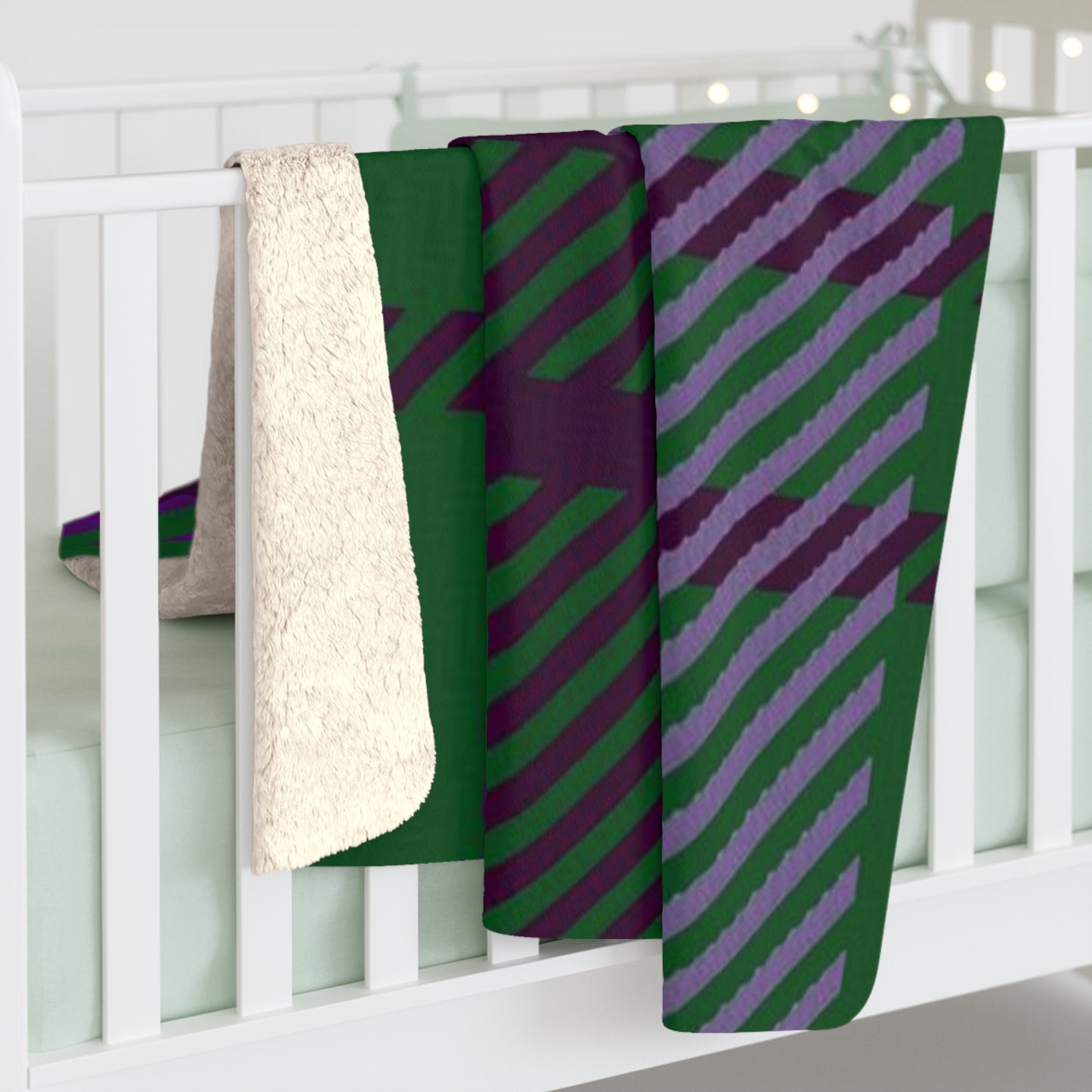 A folded baby blanket draped over a white crib, showing a green and purple diagonal striped pattern on one side and a soft cream sherpa fleece backing on the other.