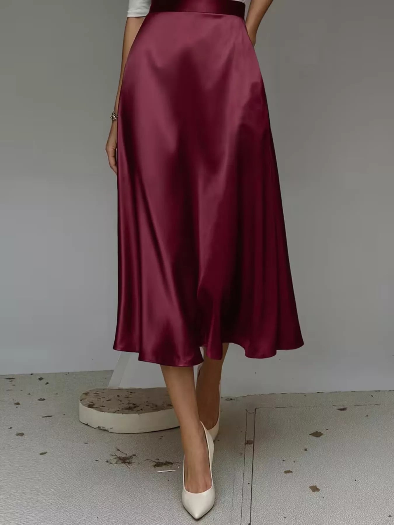 Person wearing a burgundy satin skirt with white shoes on a plain background