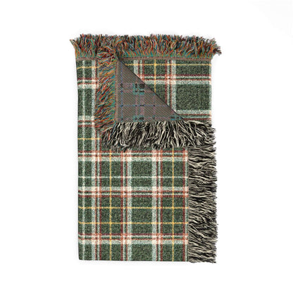 A folded plaid throw blanket with fringed edges, featuring a green, white, and red tartan pattern with a gray reverse side, shown on a plain white background.