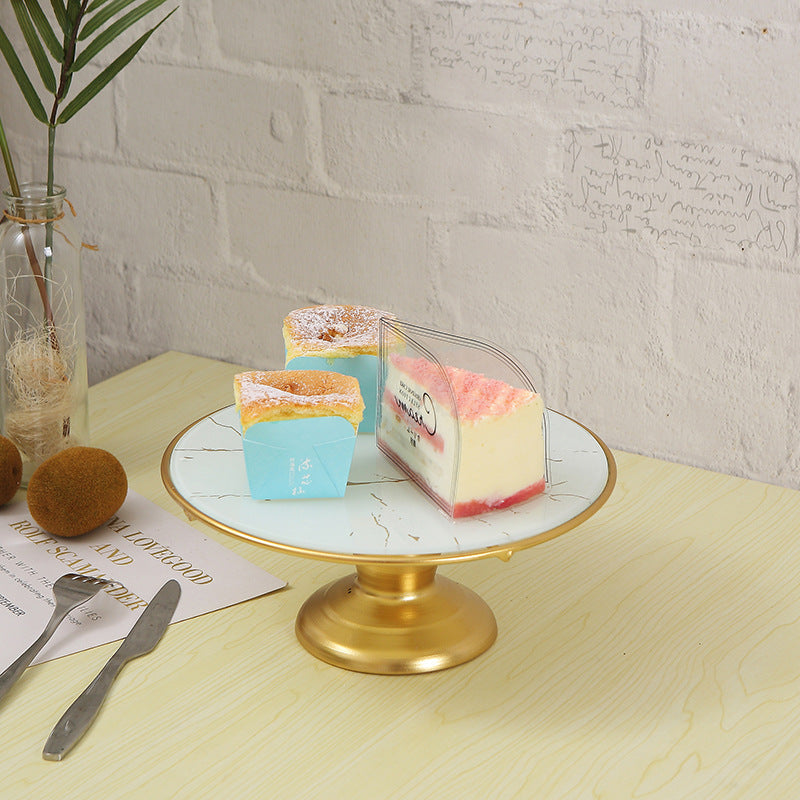 Three small cake slices on a marble stand with a gold base, against a light brick wall.