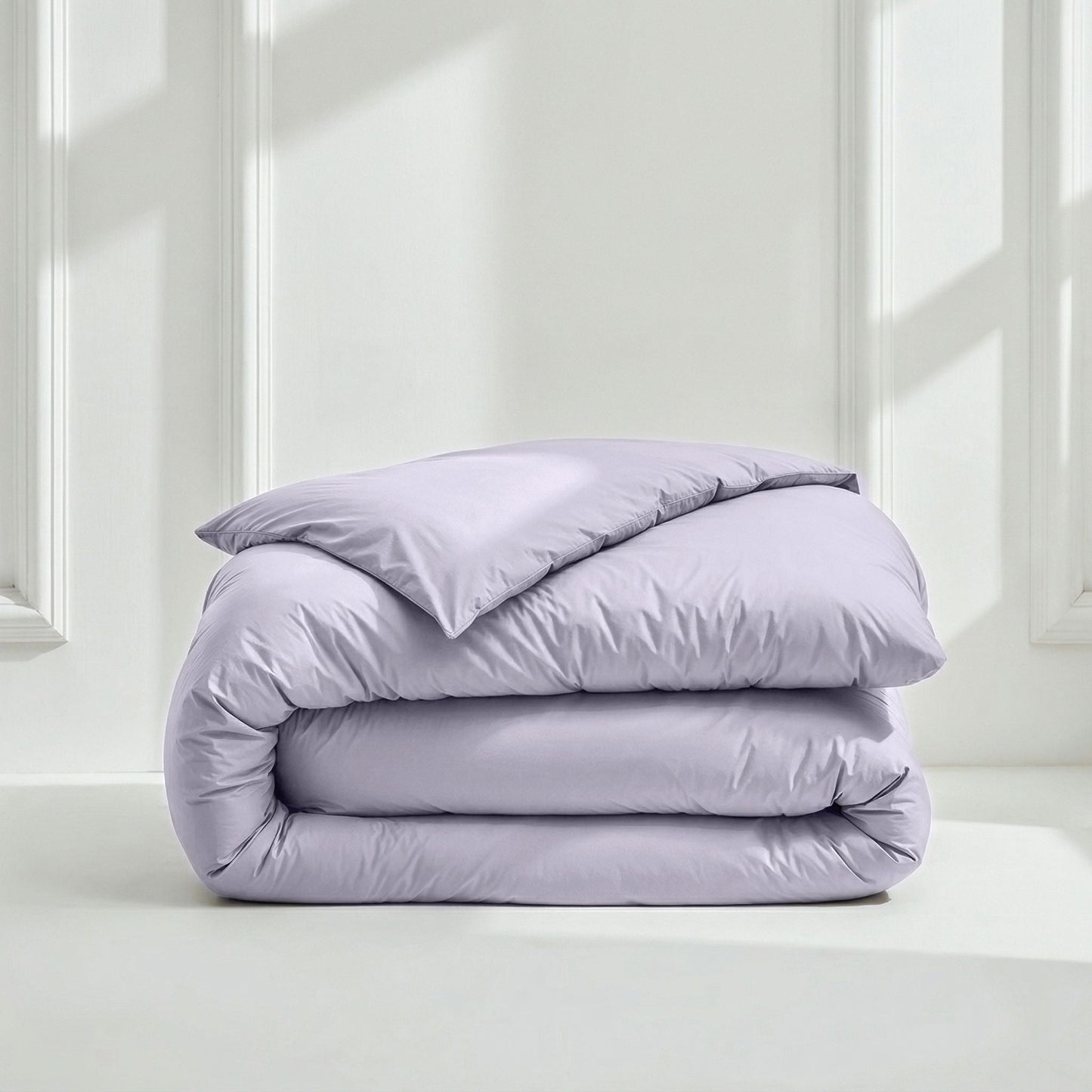Folded lavender comforter on a white surface with a light gray wall background