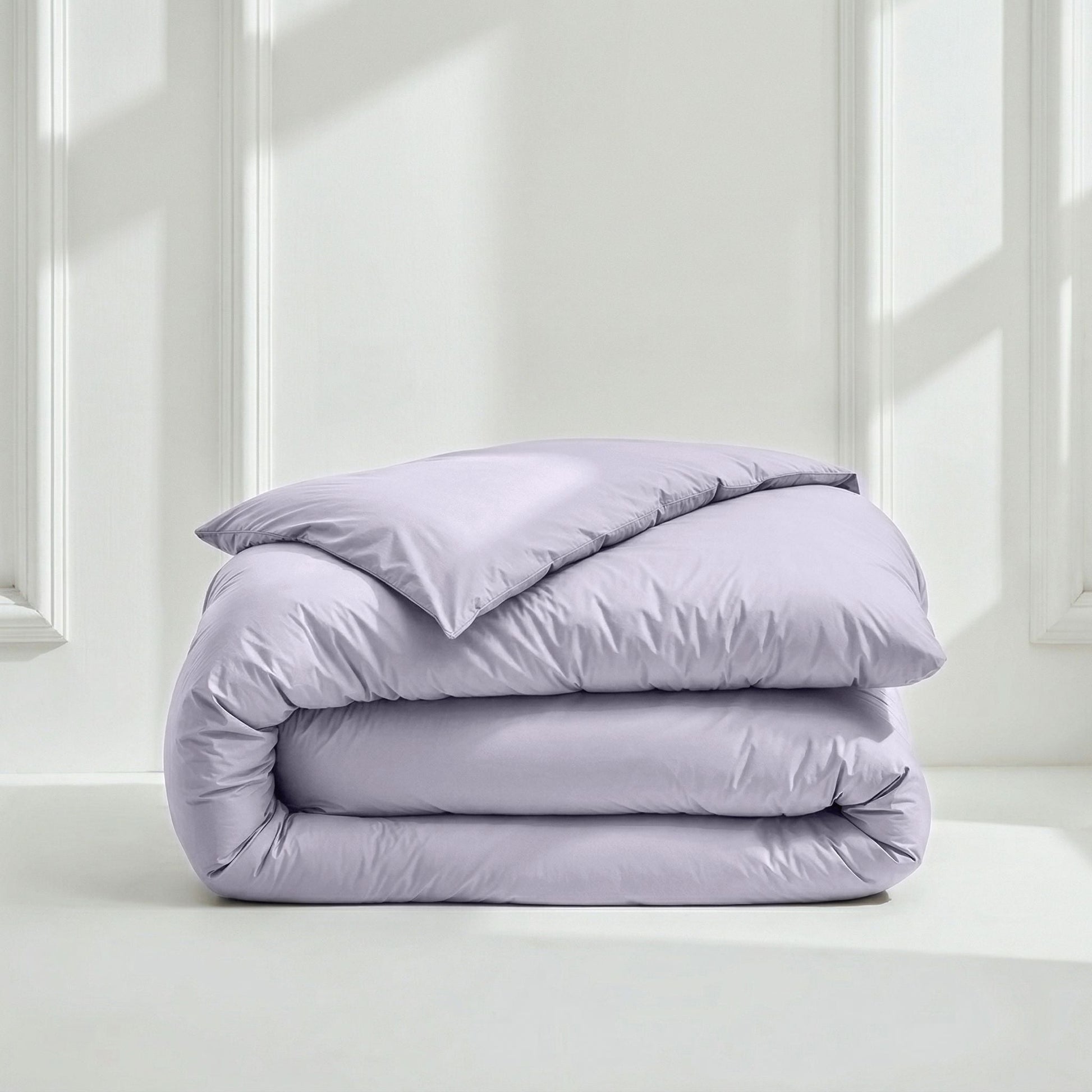 Folded lavender comforter on a white surface with a light gray wall background