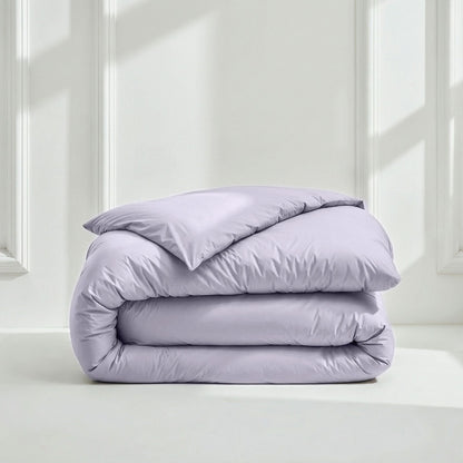 Folded lavender comforter on a white surface with a light gray wall background