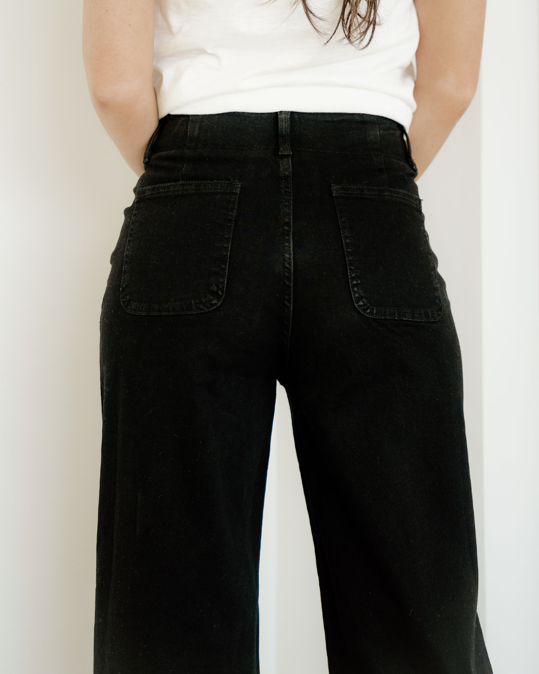 Person wearing black high-waisted jeans with a plain background