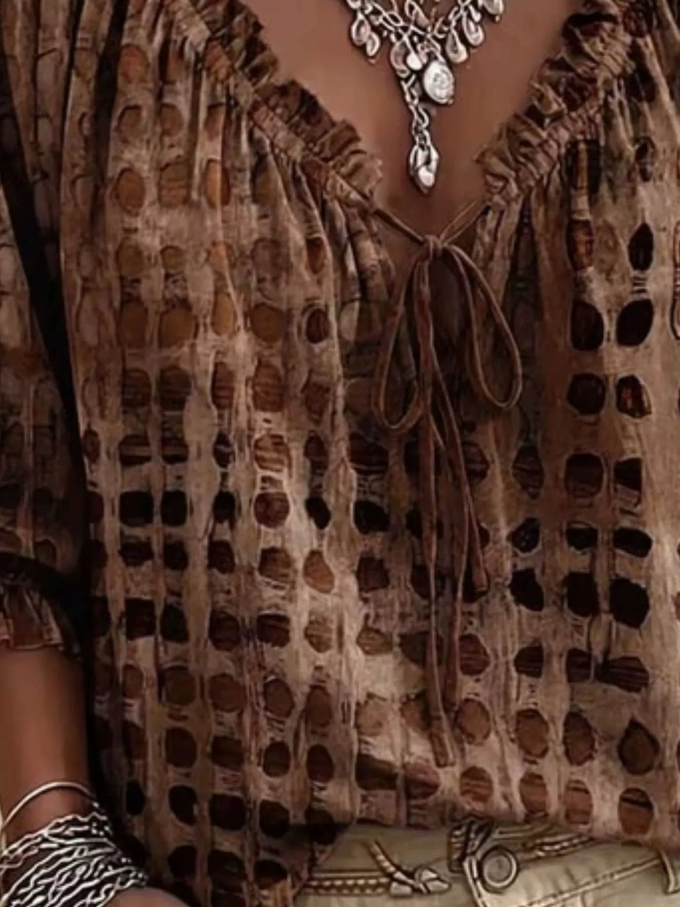 Close-up of a brown bohemian-style top with a distressed, perforated pattern, featuring a ruffled V-neckline with a tie closure and a tie-dye effect.
