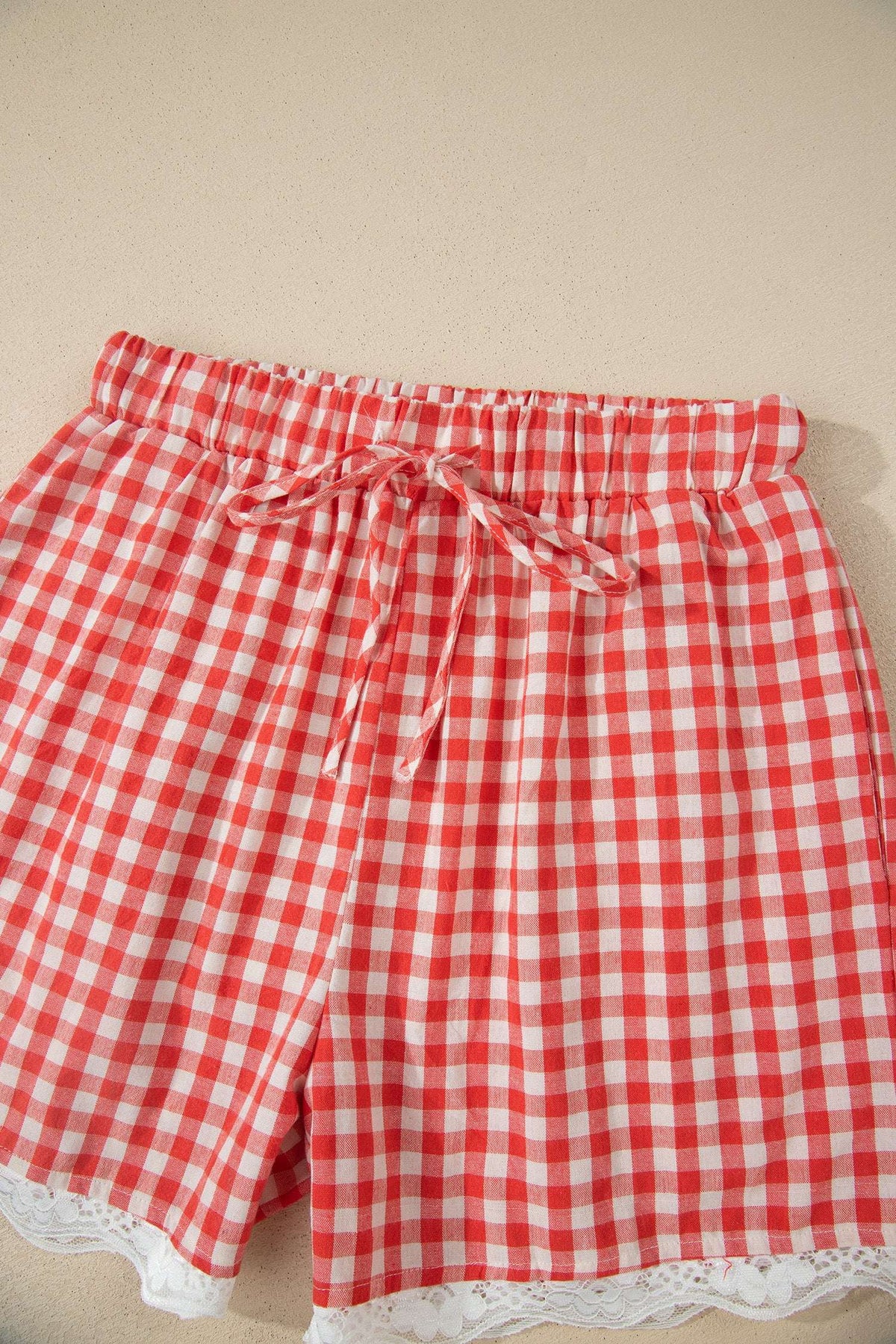 Red and white gingham fabric shorts with an elastic drawstring waist and white lace trim at the hem.