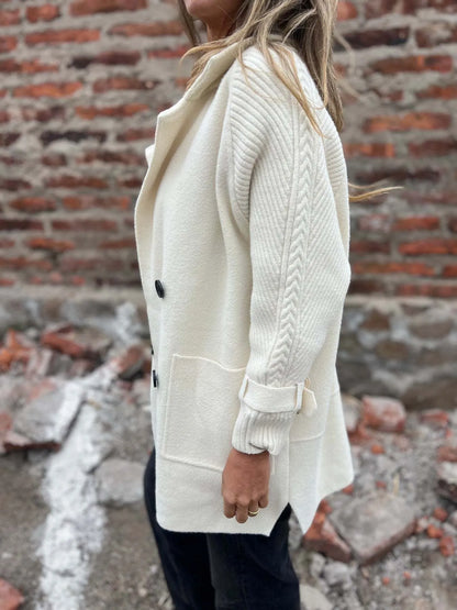 Model wearing a white double-breasted coat with cable-knit sleeves, buckled cuffs, wide lapels and front pockets.