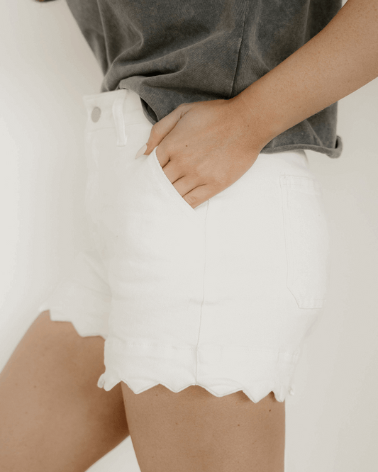 Woman wearing white denim scalloped hem shorts. Side view.