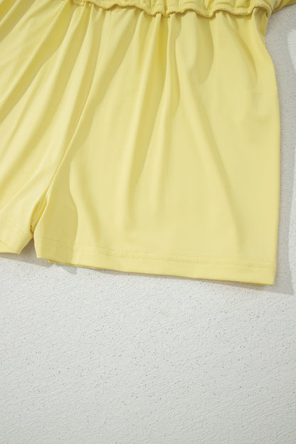Close-up of a light yellow garment, showing the gathered waistband and upper leg portion, laid against a textured off-white background.