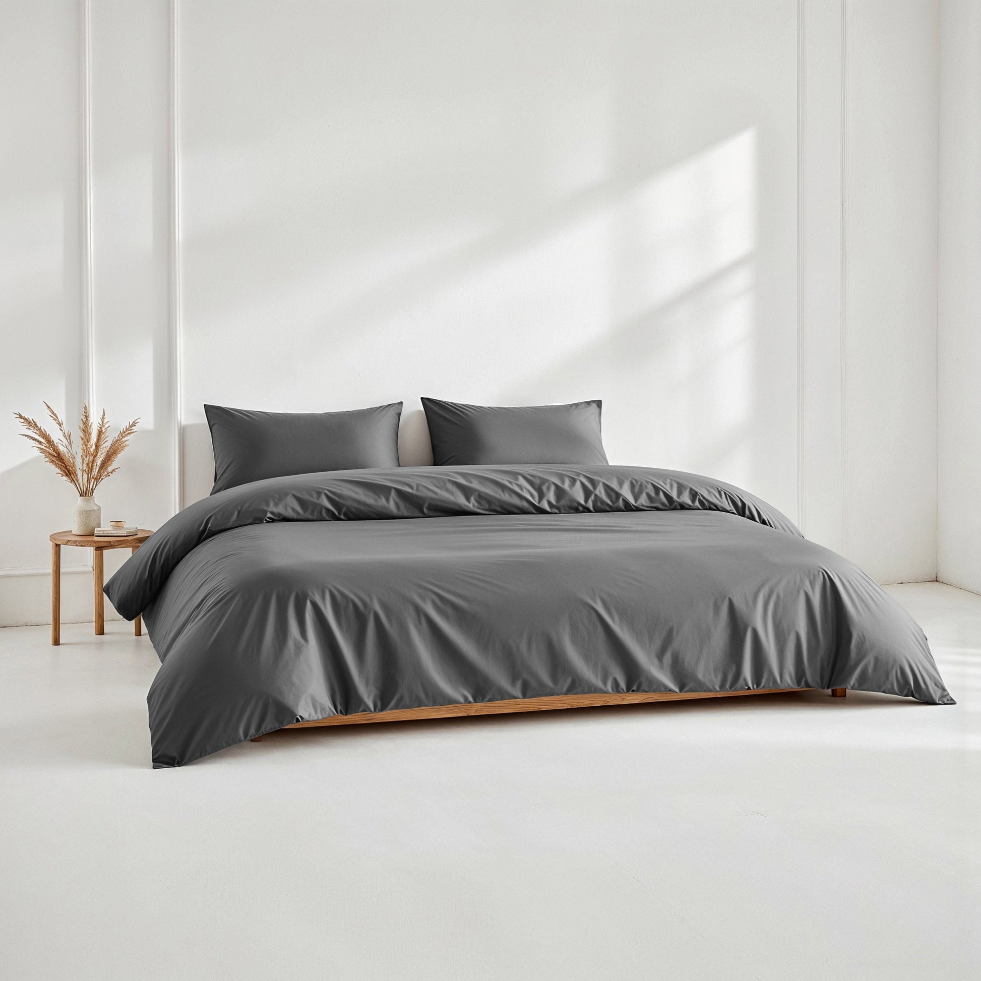 Gray bedding set on a bed in a minimalistic room with a side table and plant.