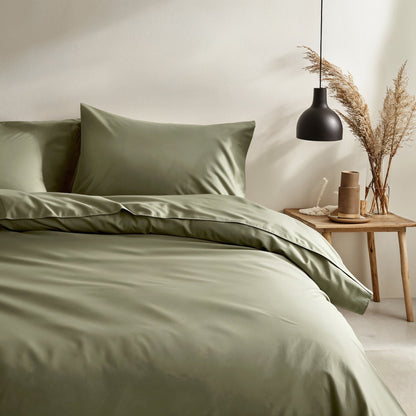 Green bedding set on a bed in a bedroom with a side table and decorative elements.