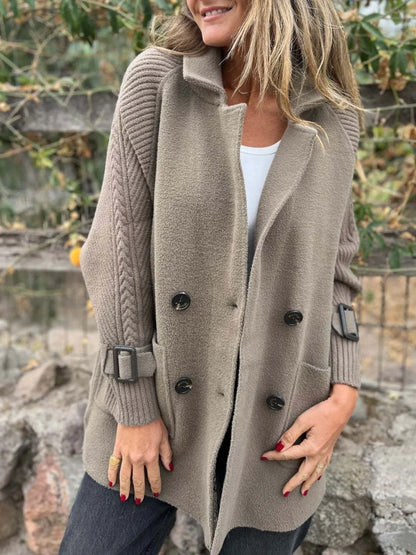 Model wearing a mocha double-breasted coat with cable-knit sleeves, buckled cuffs, wide lapels and front pockets.