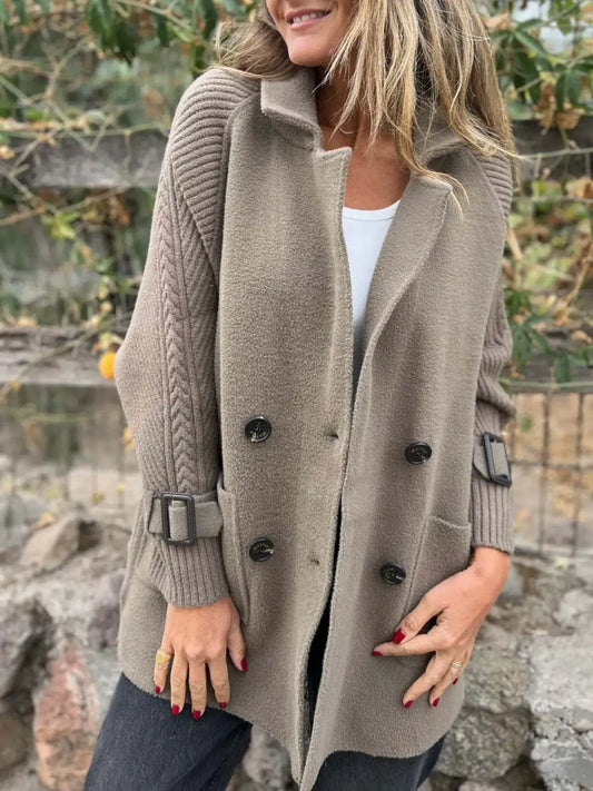 Model wearing a mocha double-breasted coat with cable-knit sleeves, buckled cuffs, wide lapels and front pockets.