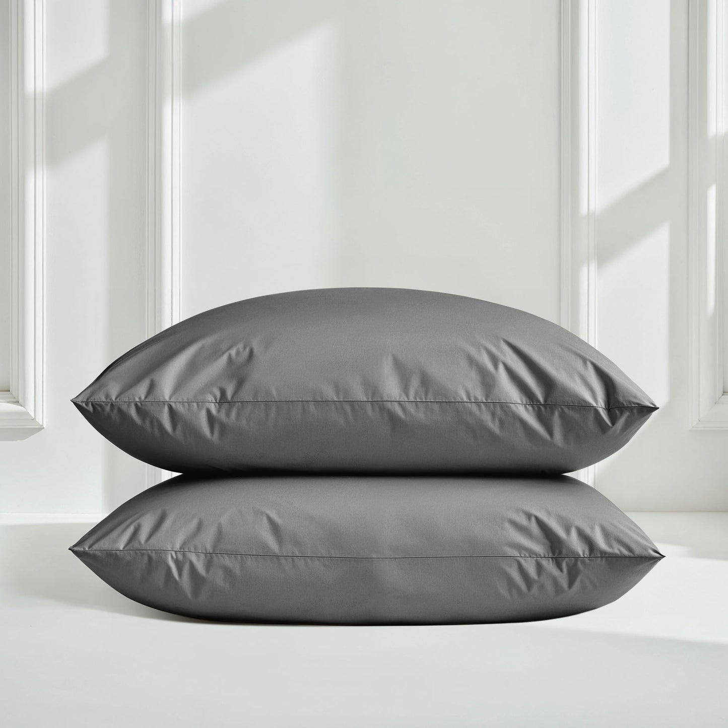 Two gray pillows on a white surface with a neutral background