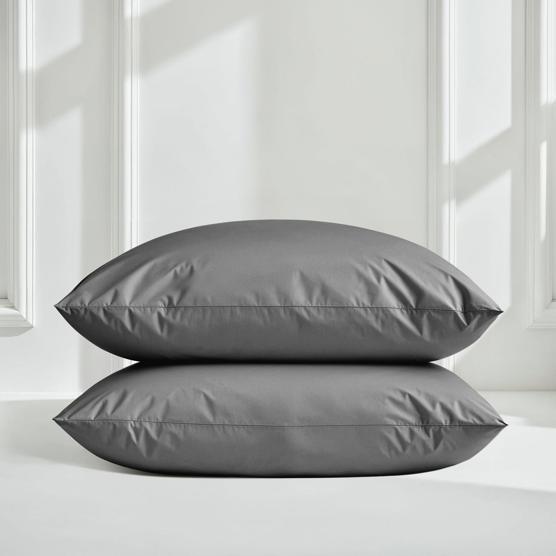 Two gray pillows on a white surface with a neutral background