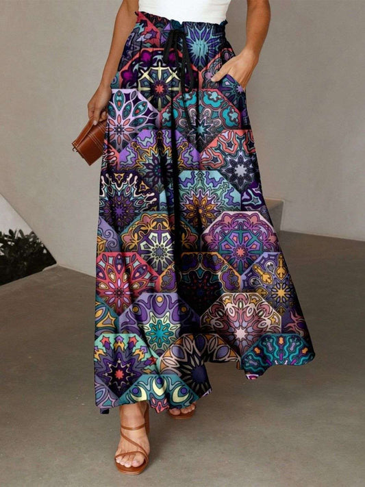 A model wearing a multicolored printed maxi skirt with pockets, paired with a sheer top and sandals.