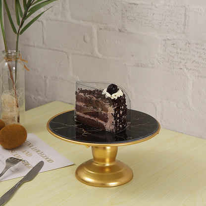 Slice of chocolate cake on a black marble cake stand with gold base, placed on a light wooden table.