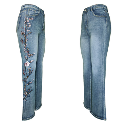 A pair of light blue denim jeans shown from the front and back. The back view features a vertical floral embroidery design in pink, purple, and black thread running down the left leg.