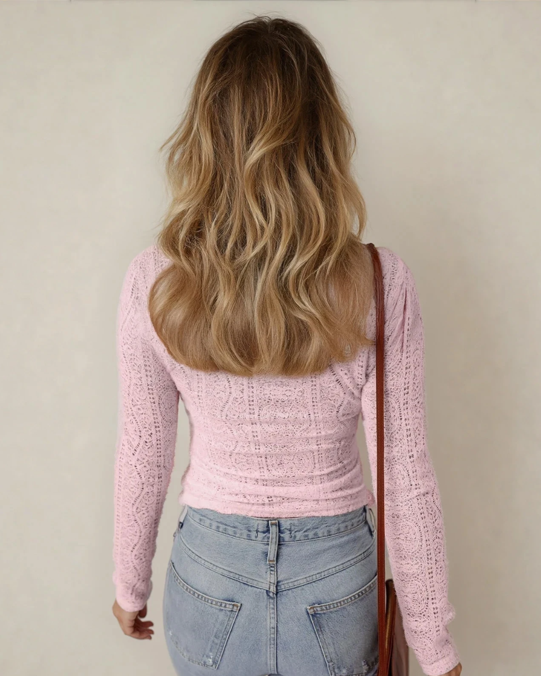 Person wearing a pink knitted sweater and blue jeans with a neutral background