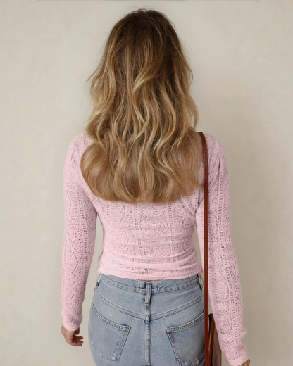 Person wearing a pink knitted sweater and blue jeans with a neutral background
