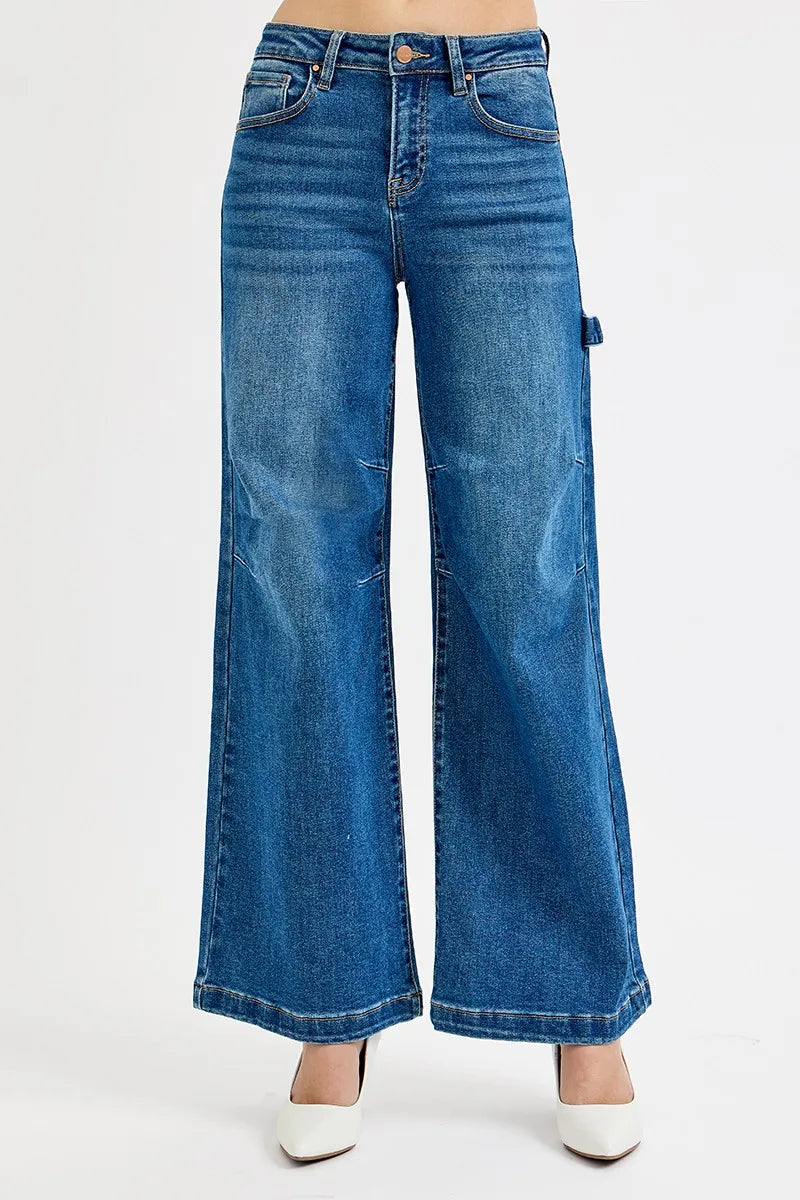 A person wearing blue wide-leg denim jeans with a faded wash and white pointed-toe heels, shown from the waist down on a plain light background.