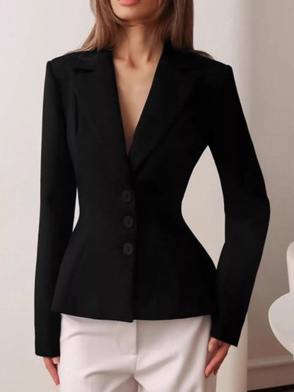 A woman wearing a fitted black blazer with structured shoulders, a deep V-neckline, and three front buttons, paired with white pants.