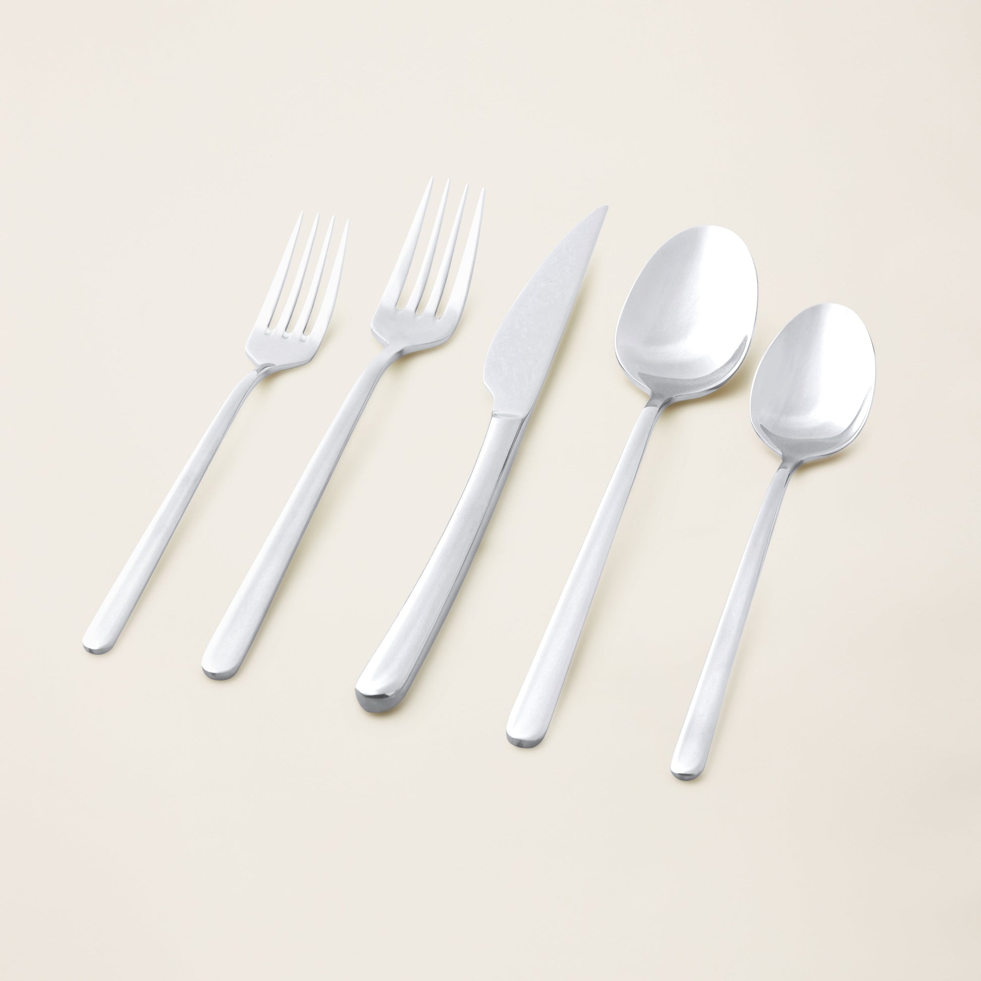 Set of silver cutlery including forks, a knife, and spoons on a light beige background.