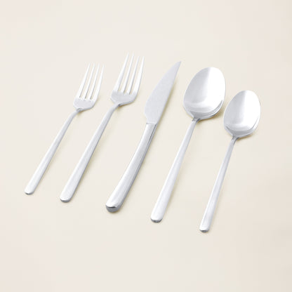 Set of silver cutlery including forks, a knife, and spoons on a light beige background.
