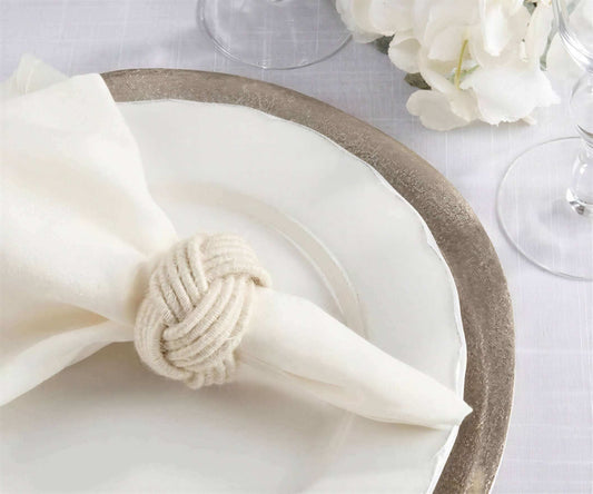 Ivory braided jute napkin ring in a knot shape on a white fabric napkin and ceramic plate.