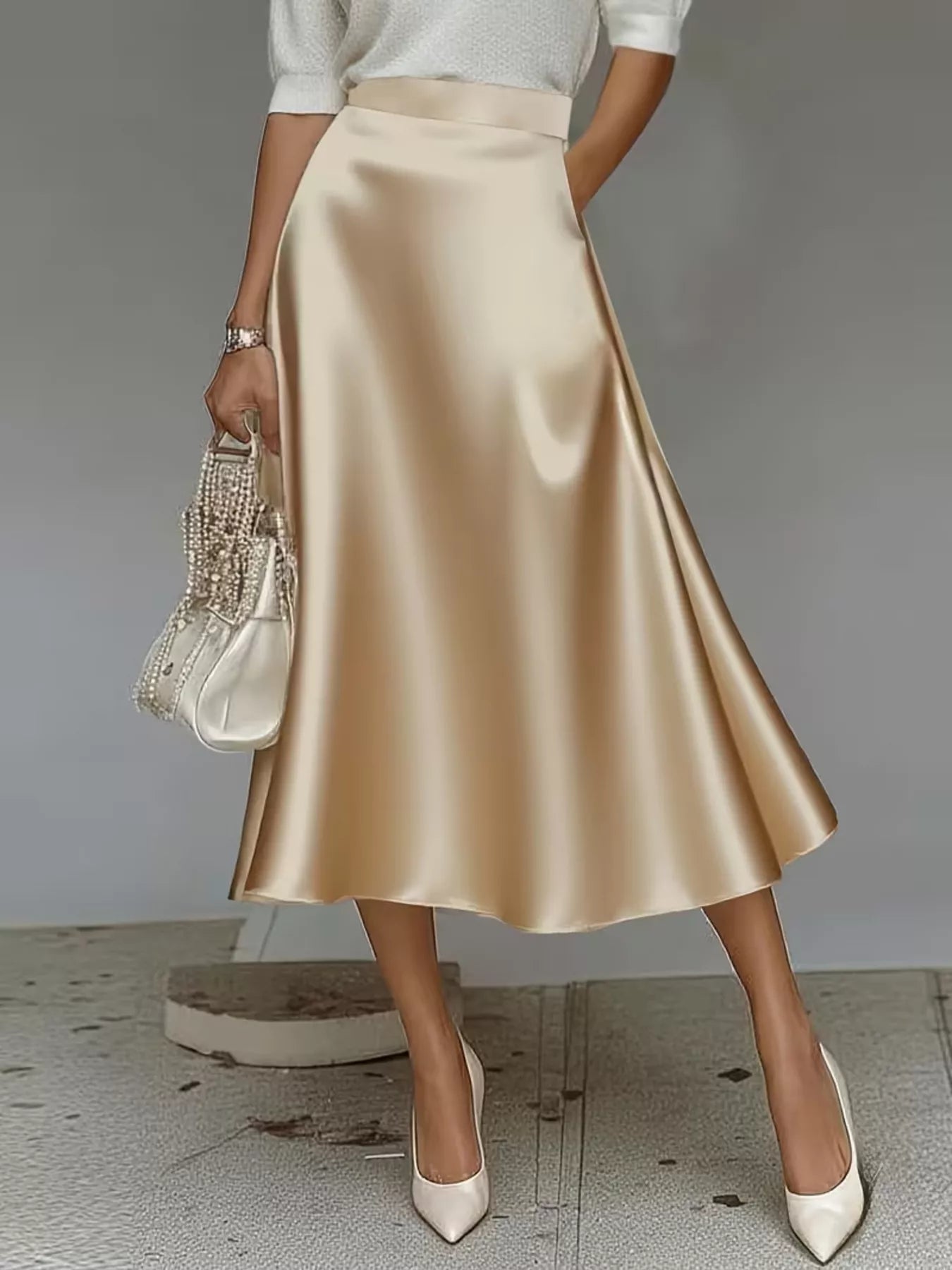 Person wearing a beige satin skirt with white shoes and a beaded handbag on a neutral background