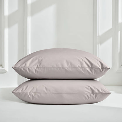 Two rectangular pillowcases stacked vertically on a white surface against a white paneled wall with soft window light shadows.