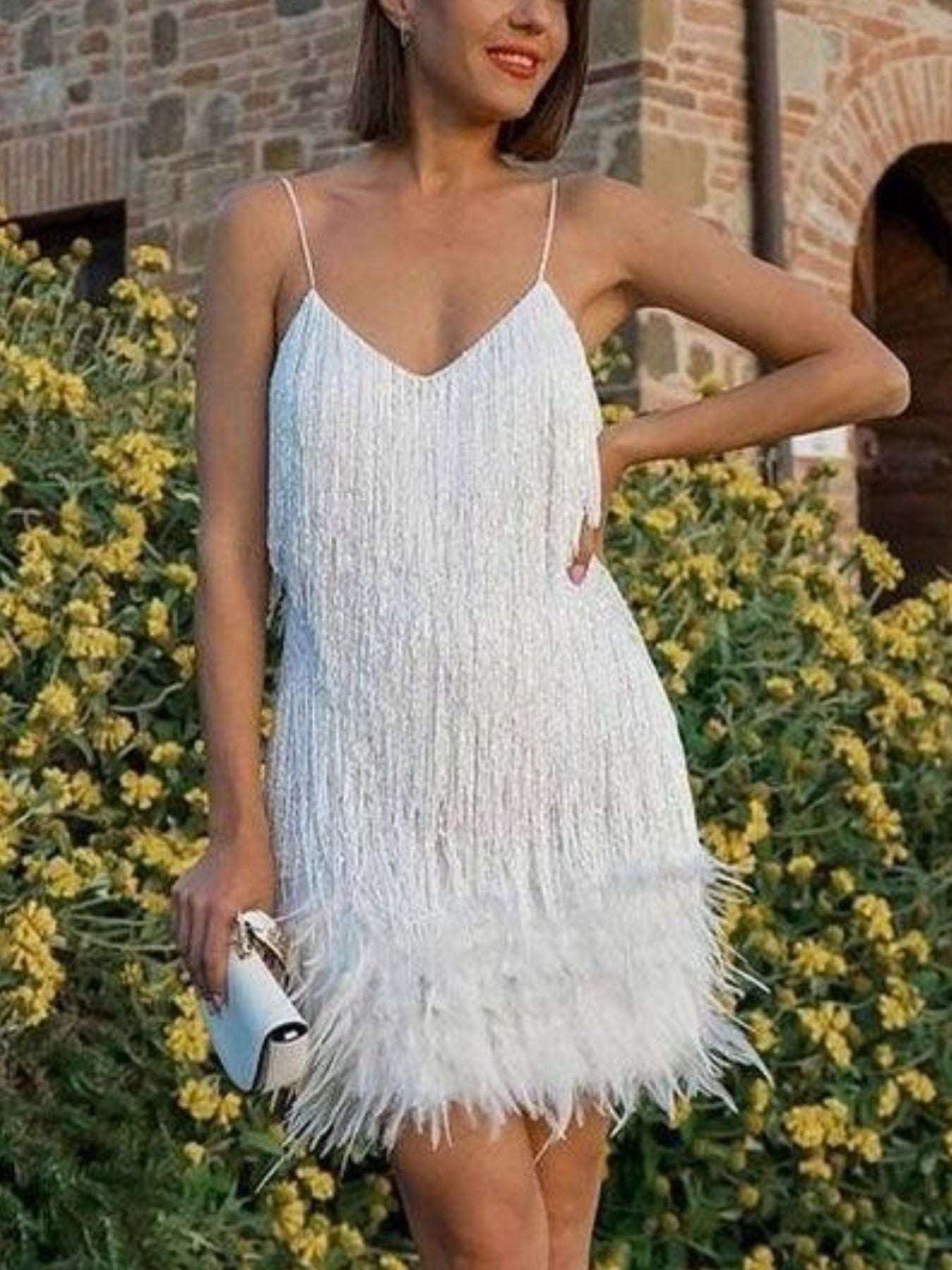 Woman wearing a white fringe dress standing in front of yellow flowers and a brick wall.