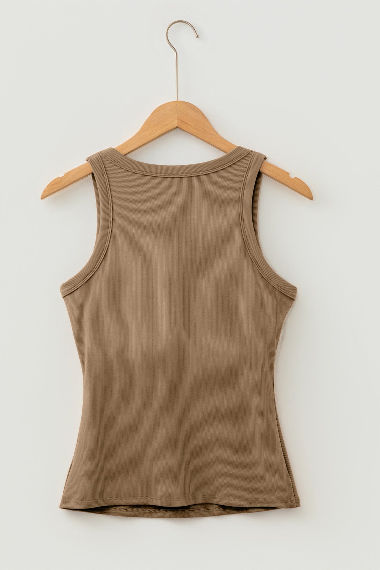 Brown ribbed fabric tank top hanging on a wooden hanger against a white wall.