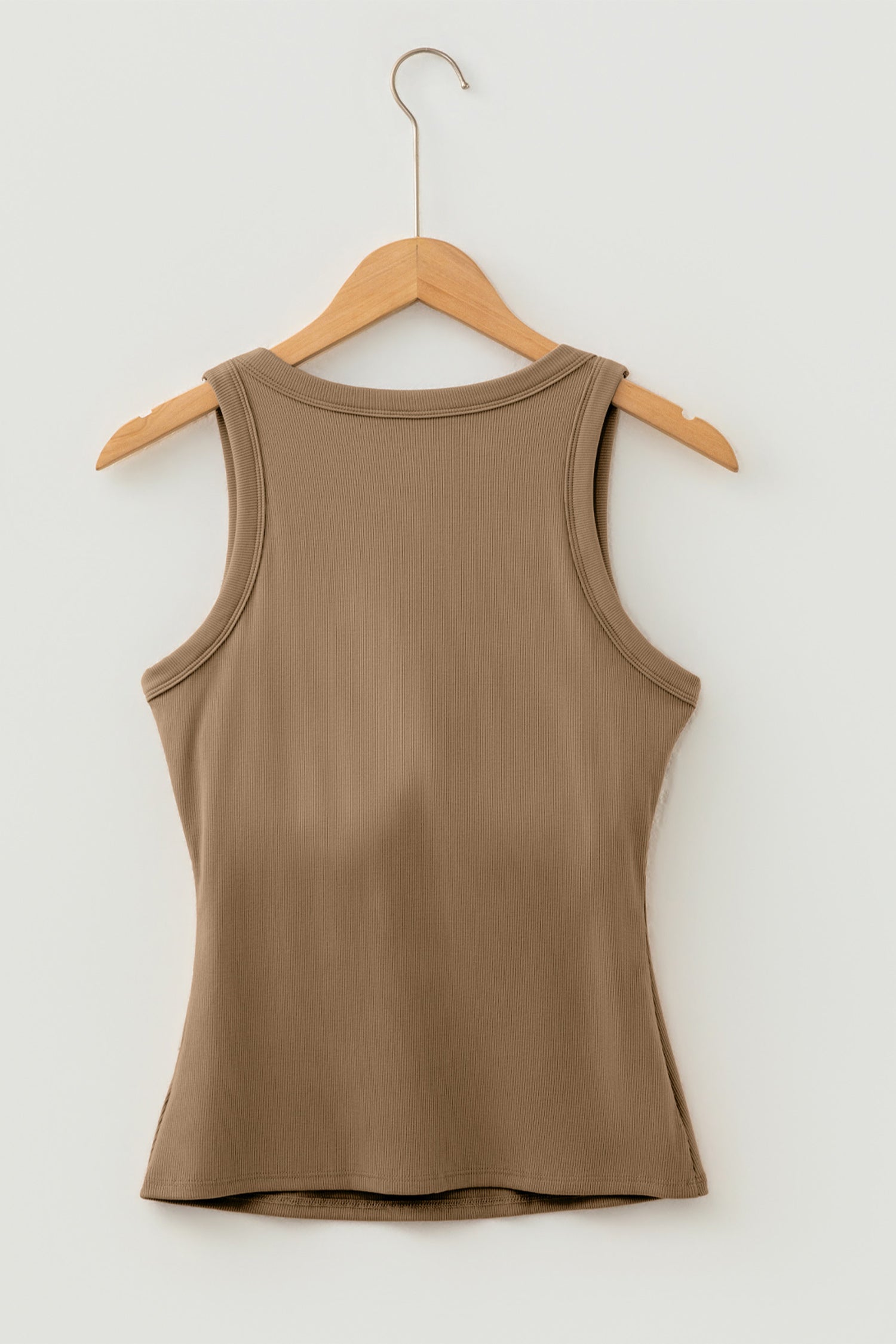 Brown ribbed fabric tank top hanging on a wooden hanger against a white wall.