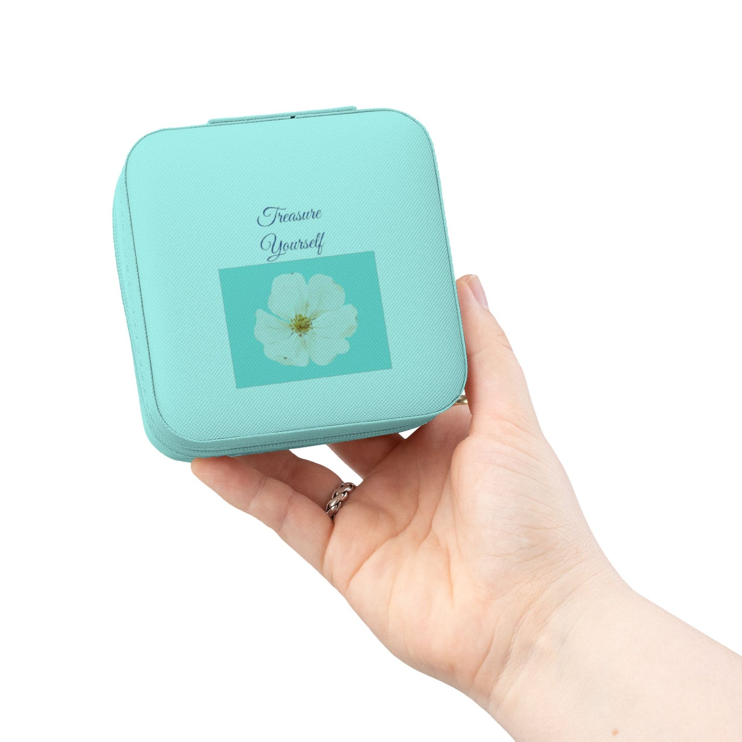 A hand holding a small mint green square compact case with a white flower graphic and the words 'Treat Yourself' on the front, against a plain white background.