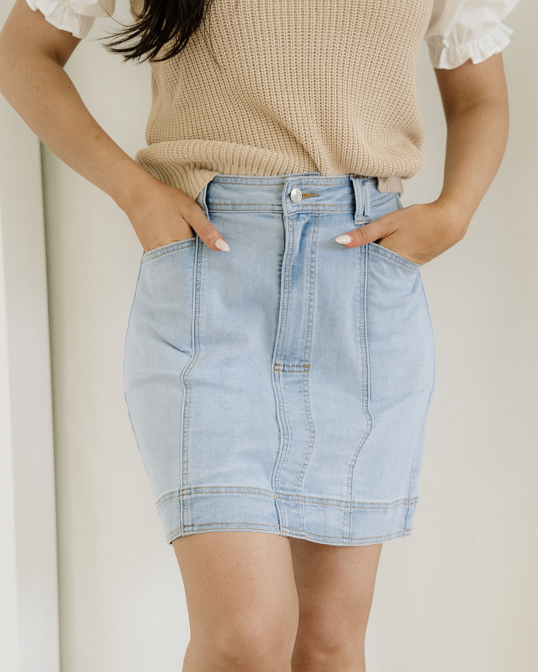 Person wearing a light blue denim skirt and beige sweater against a neutral background