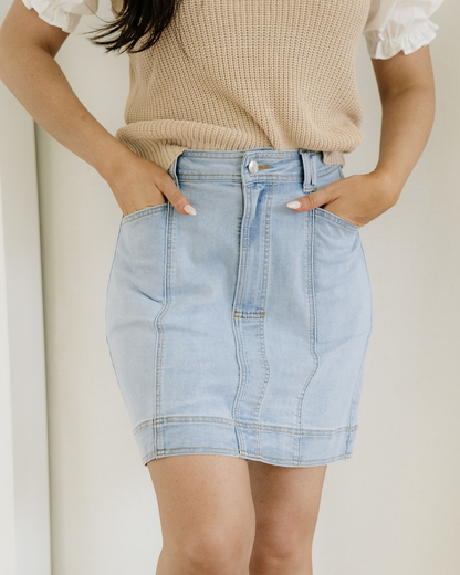 Person wearing a light blue denim skirt and beige sweater against a neutral background