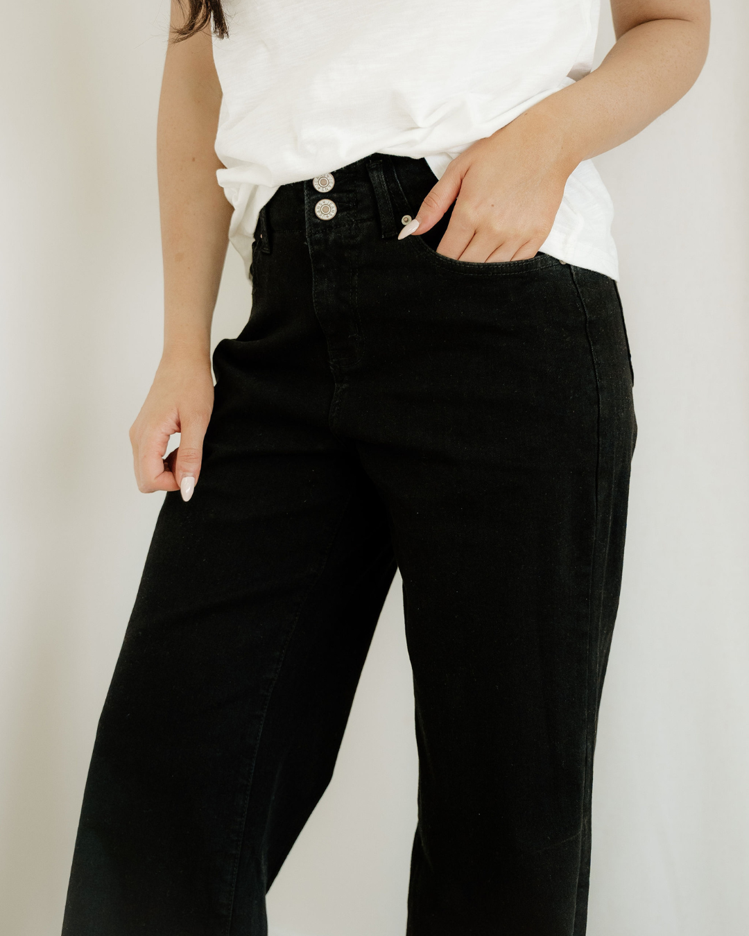 Person wearing black pants with a white top on a plain background